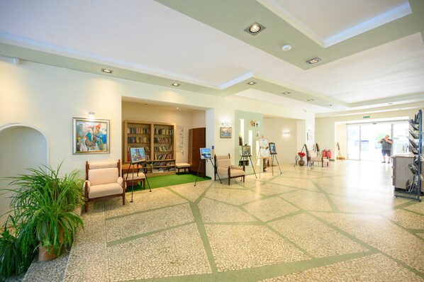 A spacious lobby with a central seating area, a bookshelf, and artwork on display. - International House of Journalists (Varna)