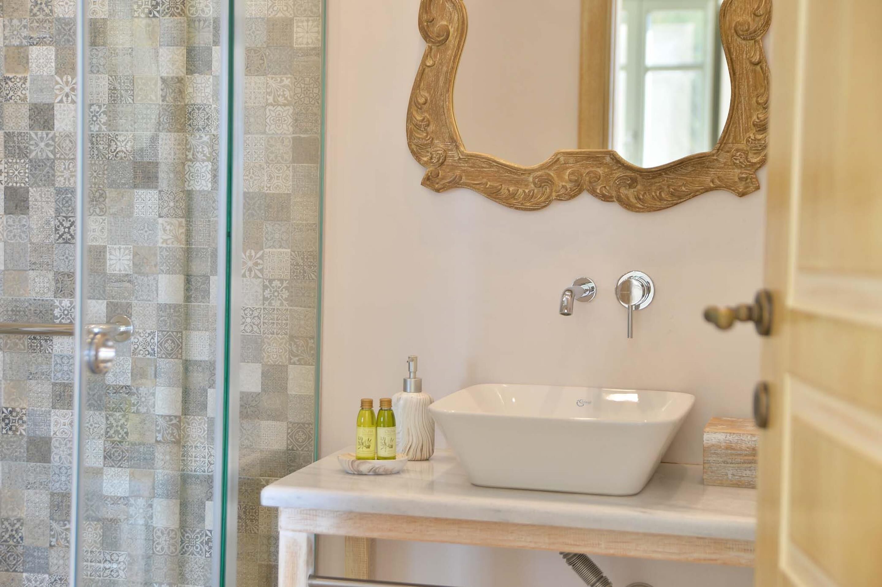 Un baño con un lavamanos blanco, un espejo con un marco decorativo y azulejos estampados en las paredes.