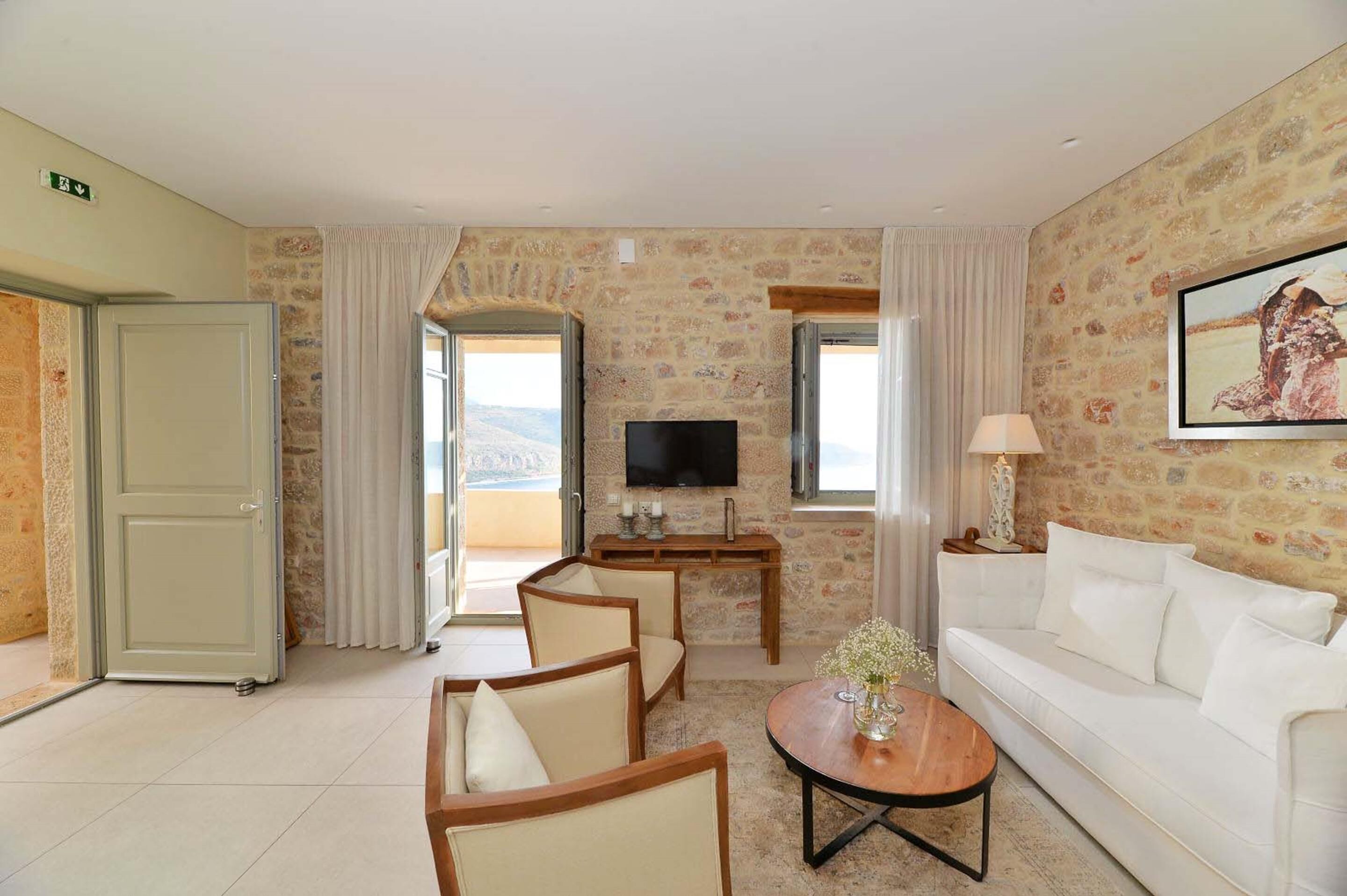 A spacious living room with a stone wall, a flat-screen TV, a white sofa, and a wooden coffee table.