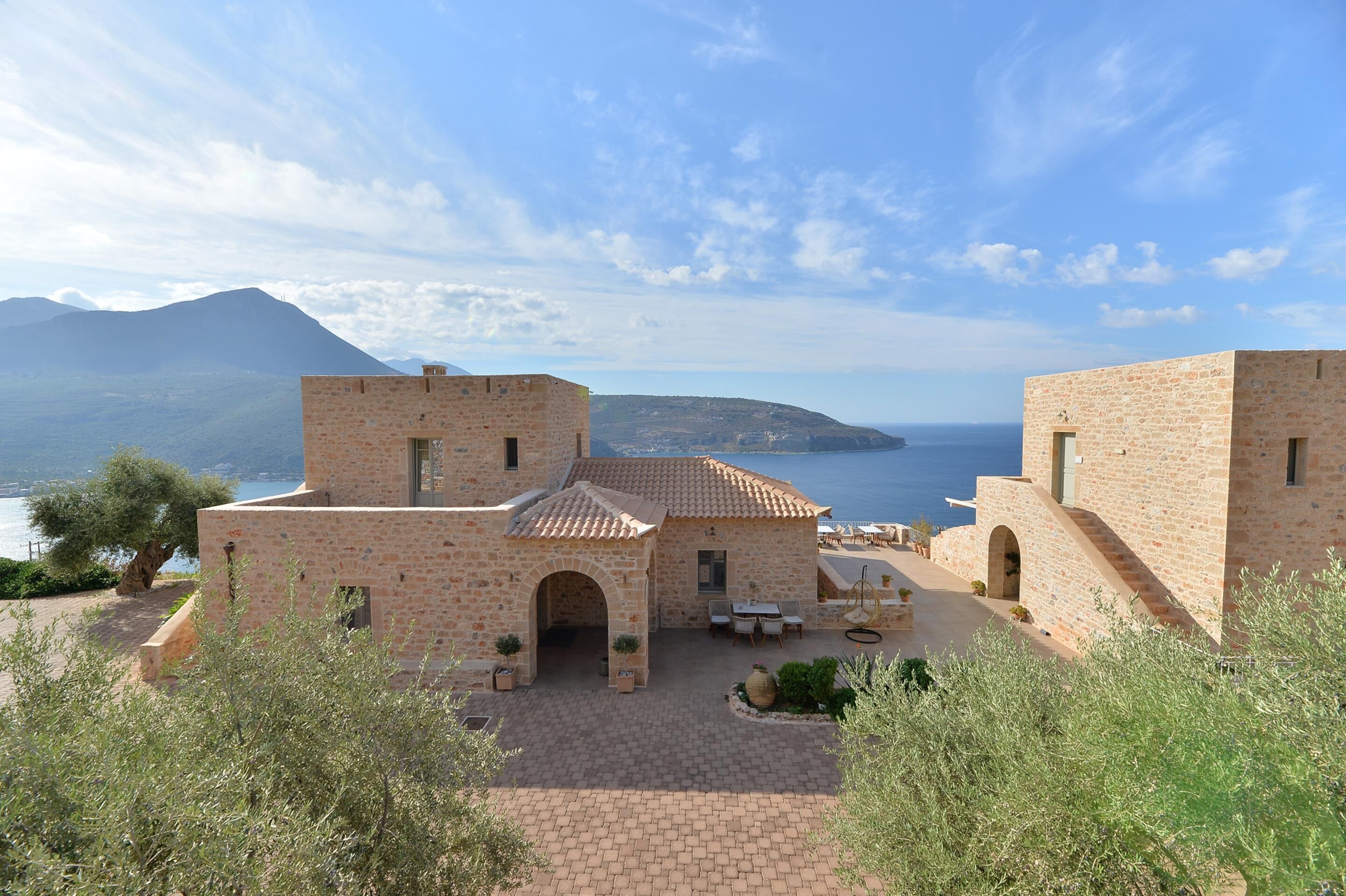 Un bâtiment en pierre doté d’une cour, d’un espace extérieur aménagé pour s’asseoir et offrant une vue sur la mer et les montagnes.