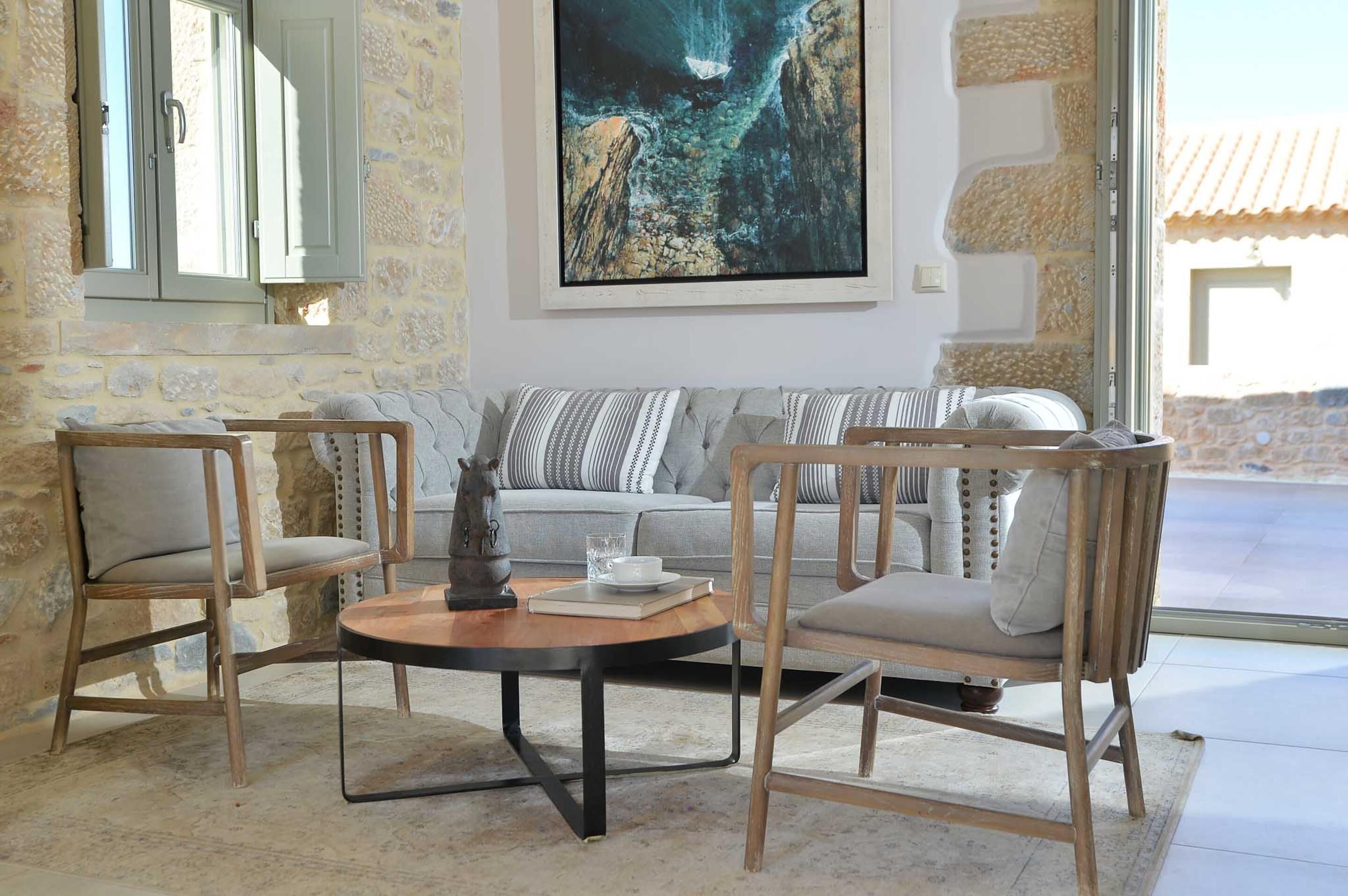 A cozy living area with a stone wall, a sofa, two wooden chairs, and a round coffee table.