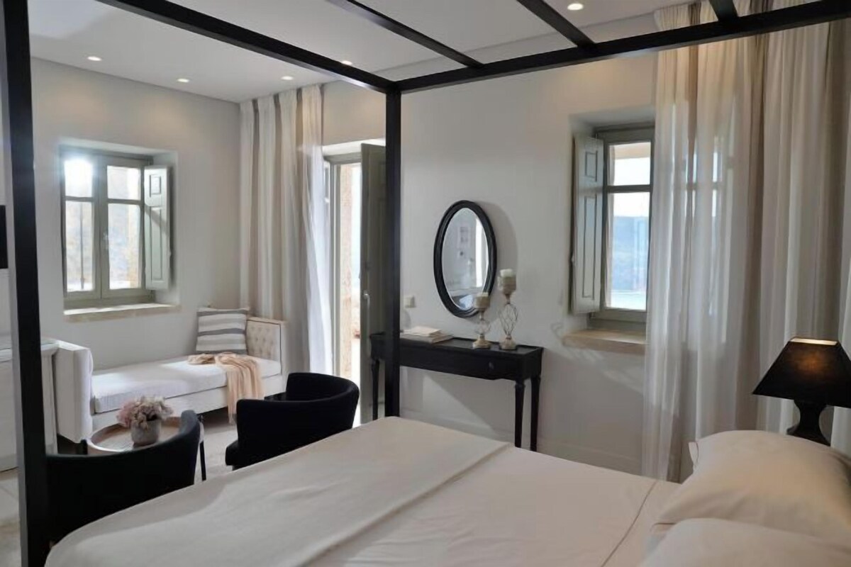 A hotel room with a bed, a desk with a mirror, a chair, a sofa, and a window with curtains.