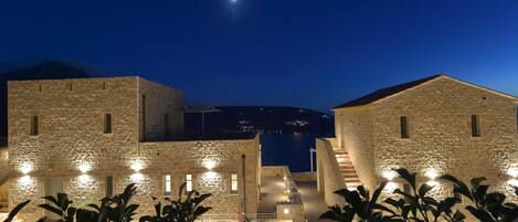 A stone building with a staircase leading to a balcony overlooking a body of water.