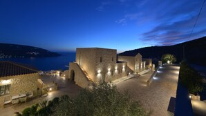 Un edificio de piedra con patio, asientos al aire libre y vista al mar al anochecer.