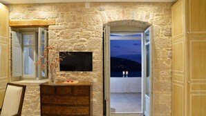 Habitación de paredes de piedra con televisor de pantalla plana, cómoda de madera y vista nocturna al exterior.