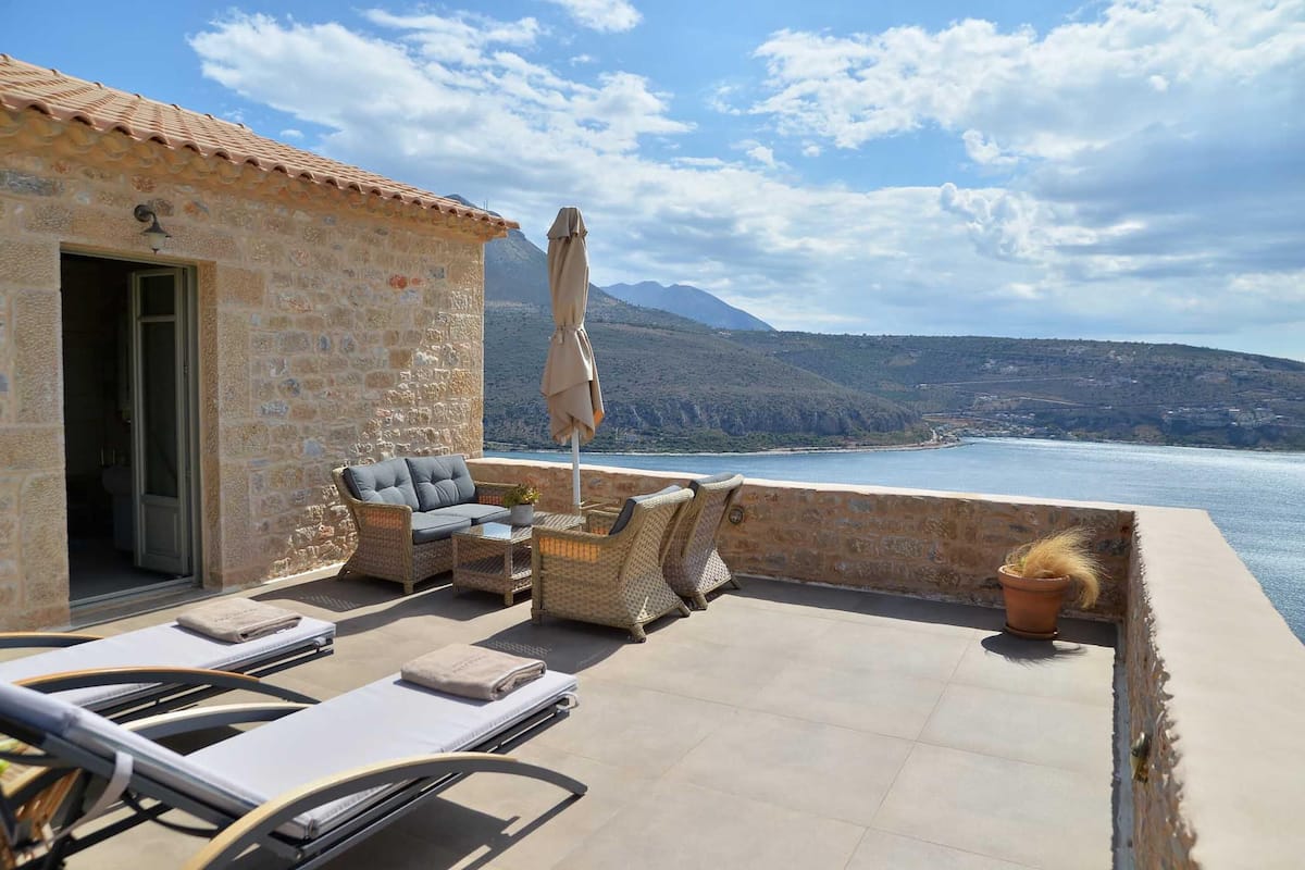 Un edificio de piedra con terraza, muebles de exterior y vista al mar.