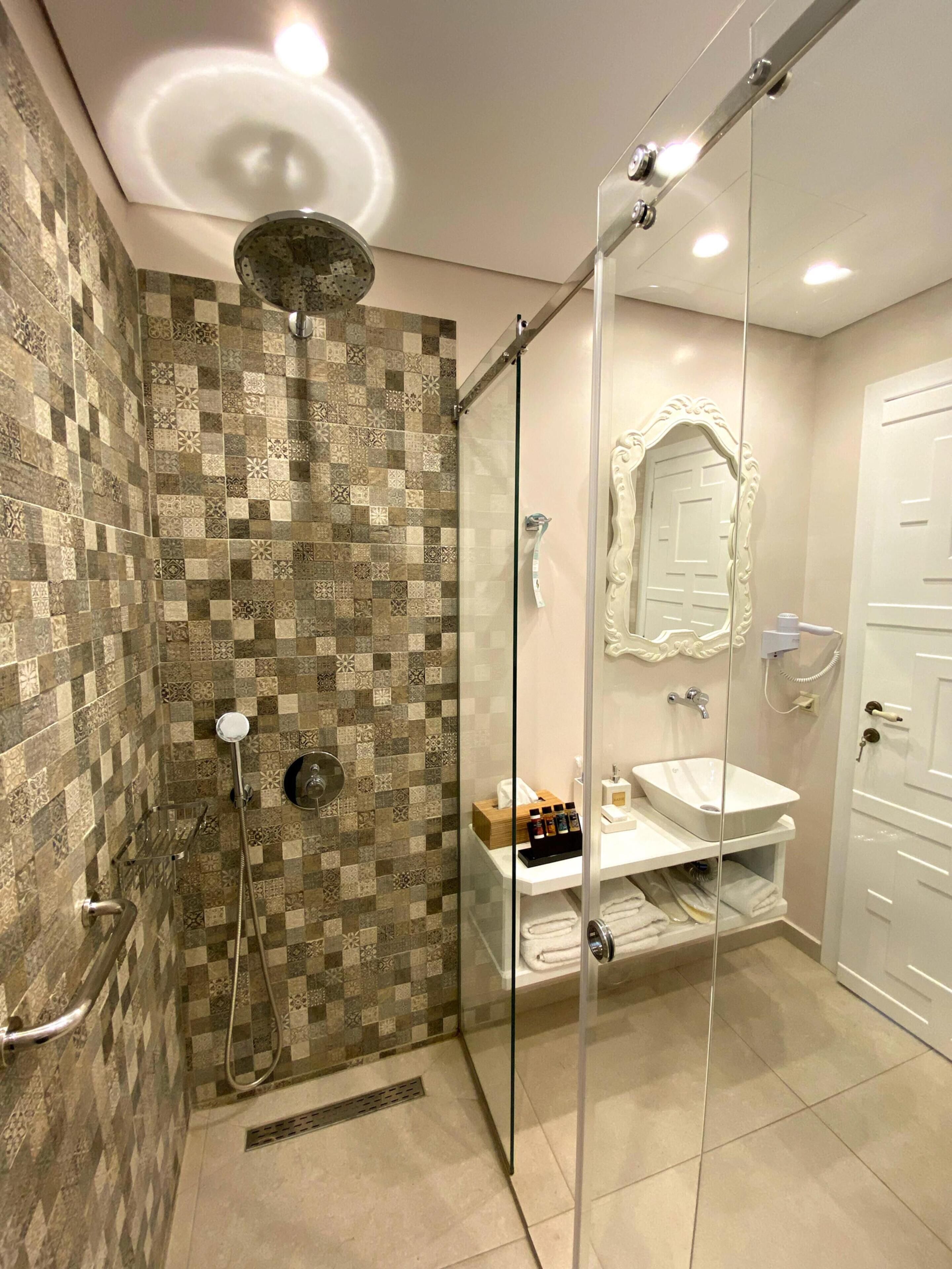 Un baño moderno con pared de baldosas a cuadros, ducha con mampara de vidrio, lavamanos blanco y espejo con marco decorativo.