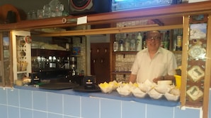A bar area with a tiled backsplash, shelves with bottles, and a counter with food items. - Sporting Baia Dependence Villa Athena (Giardini Naxos)