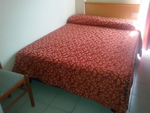 A single bed with a floral-patterned bedspread in a room with a wooden headboard and a chair. - Sporting Baia Dependence Villa Athena (Giardini Naxos)