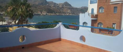 Una terraza con vistas a un pueblo costero, una montaña y una palmera.