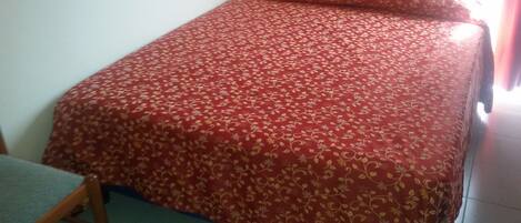 Una cama individual con una colcha de motivos florales en una habitación con cabecera de madera y una silla.