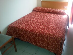 A single bed with a floral-patterned bedspread in a room with a wooden headboard and a chair. - Sporting Baia Dependence Villa Athena (Giardini Naxos)