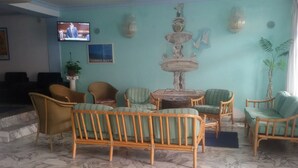 A lobby with a marble floor, wicker furniture, a fountain, and a television displaying news. - Sporting Baia Dependence Villa Athena (Giardini Naxos)