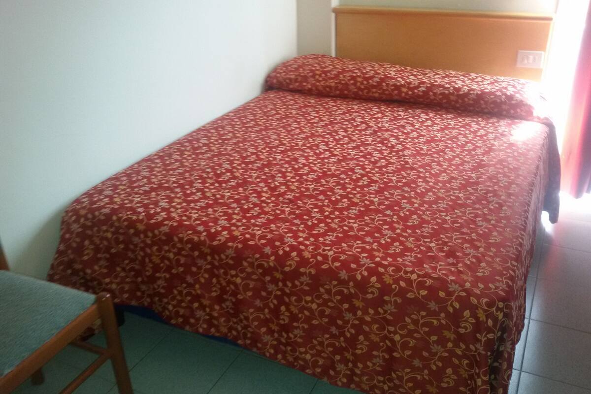 A single bed with a floral-patterned bedspread in a room with a wooden headboard and a chair.