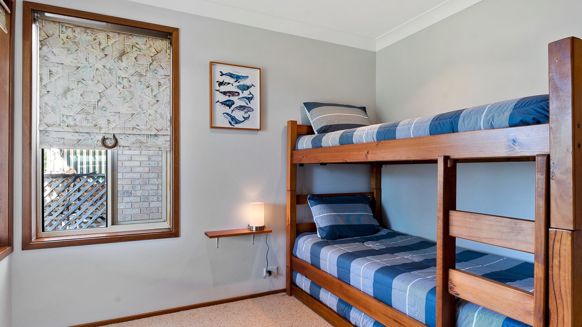 Ein Schlafraum mit Etagenbett, einem Fenster, einem gerahmten Bild von Walen und einem kleinen Nachttisch mit Lampe.