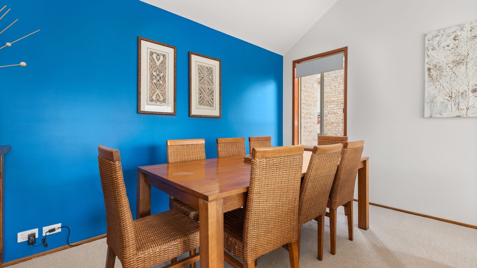 A dining room with a blue wall, a wooden table, and wicker chairs.