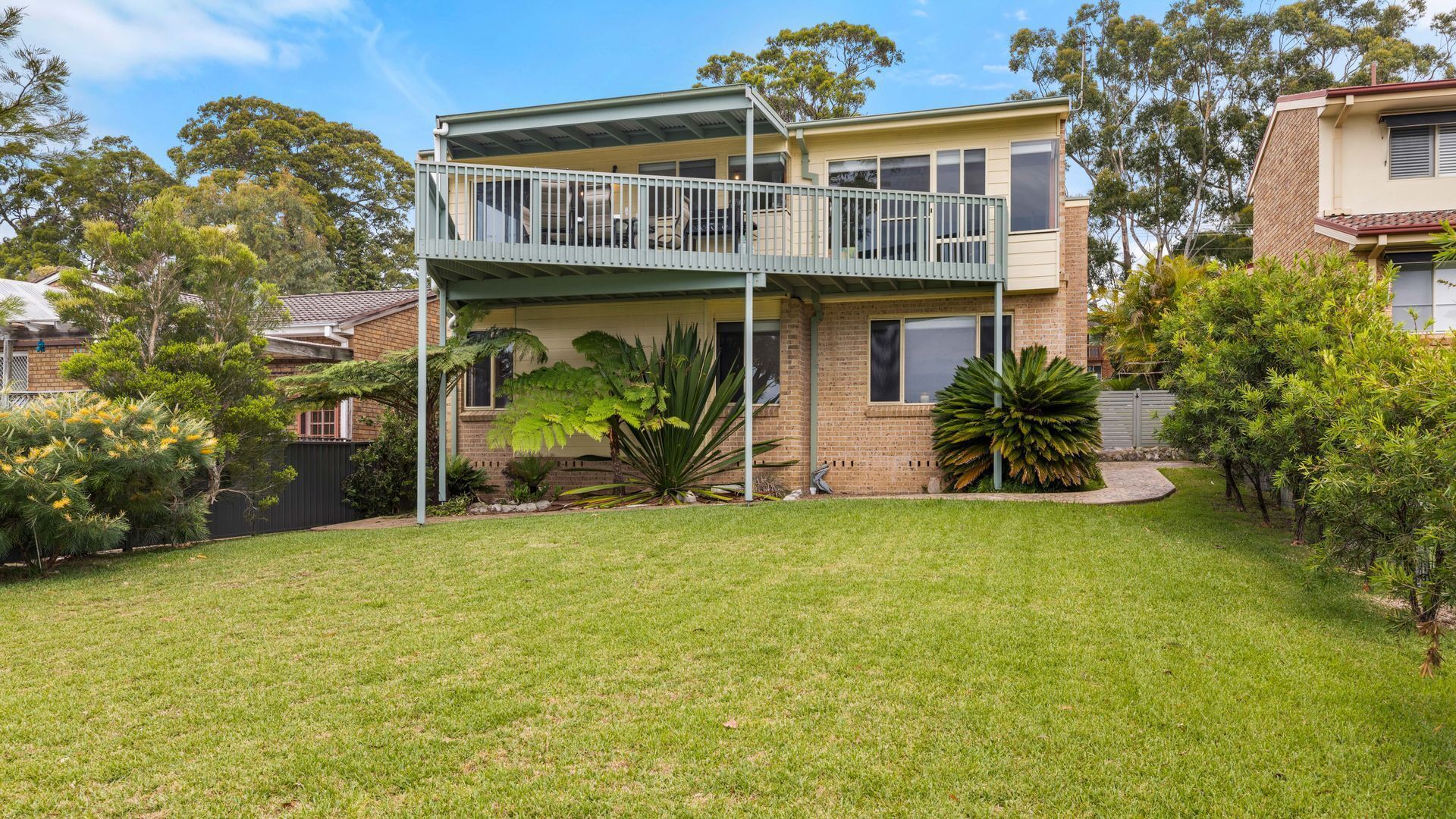 A two-story house with a balcony, surrounded by a well-maintained lawn and various plants.
