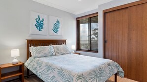 A bedroom with a bed, two bedside tables, a nightstand, a window with blinds, and a wooden wardrobe. - Daybreak by Experience Jervis Bay (Vincentia)