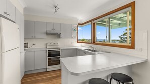 A modern kitchen with white cabinetry, a built-in oven, a stainless steel sink, and a large window offering a view of the outdoors. - Daybreak by Experience Jervis Bay (Vincentia)