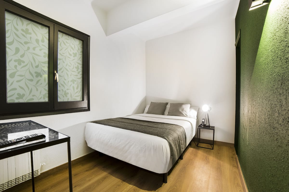A bedroom with a bed, bedside table, and a window with patterned curtains.