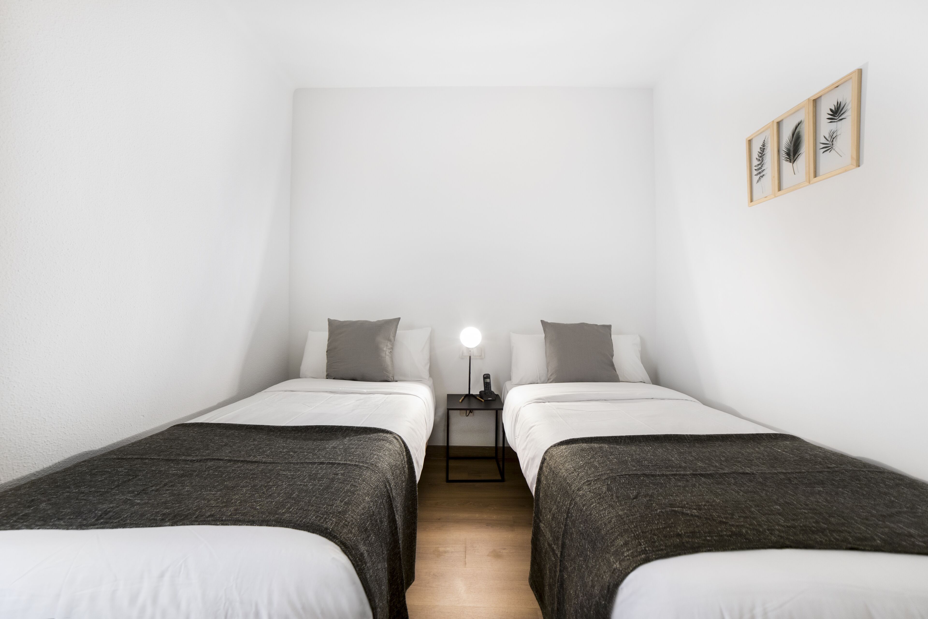 Una habitación con dos camas individuales, una mesita de noche con lámpara y un cuadro colgado en la pared.