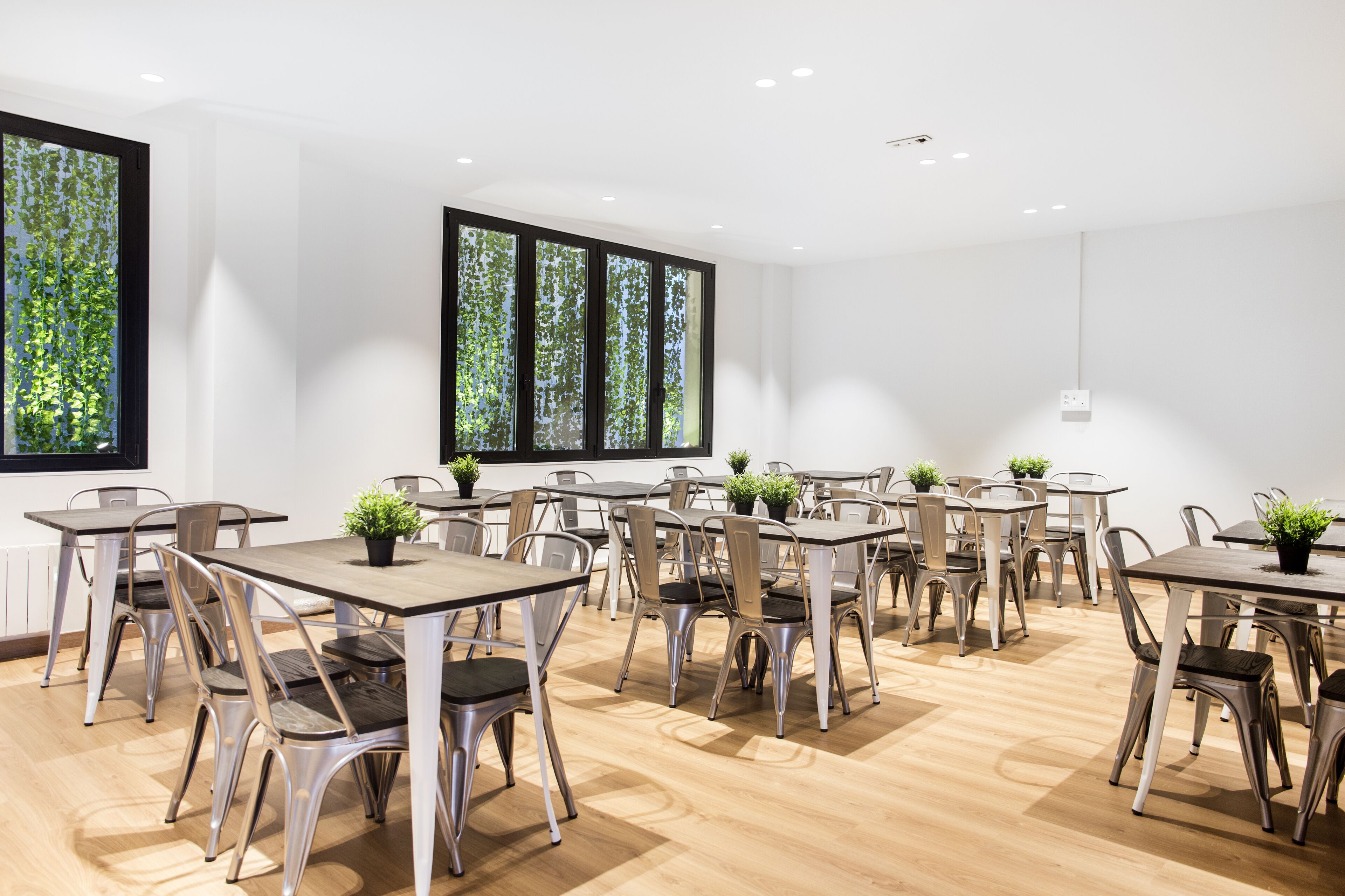 A modern dining area with multiple tables and chairs, large windows with a view of trees, and a clean, white interior.