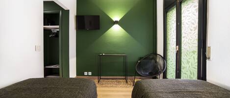 Una habitación con dos camas, una pared verde, una mesita, una silla y un televisor montado en la pared.