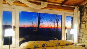 A bedroom with a large window offering a view of a sunset over a landscape. - Nido del Nibbio (Subiaco)
