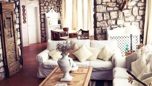 A living room with a stone wall, a white sofa, a wooden coffee table, and a dining area in the background. - Nido del Nibbio (Subiaco)
