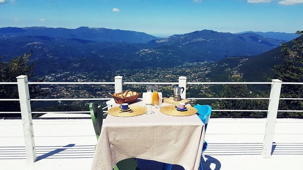 A table set with a basket of bread, a jug of orange juice, and a pitcher, overlooking a mountainous landscape. - Nido del Nibbio (Subiaco)