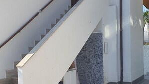 Een trap die leidt naar een deur, een betegeld terras en een muur met een structuur.