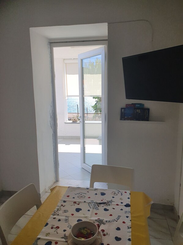 A dining area with a table set for two, a bowl of fruit, and a television mounted on the wall.