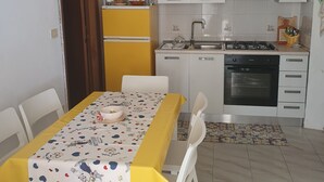 Een keuken met witte kastjes, een gele koelkast en een eettafel met een gele tafelkleed.