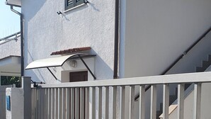 Een omheind woongebied met een wit huis, een metalen poort en een trap naar de ingang.