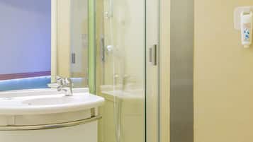 Un baño con ducha de vidrio, lavamanos blanco y un perchero para toallas.