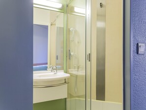 A bathroom with a glass-enclosed shower, a sink, and a mirror. - ibis budget Nantes Nord Saint-Herblain (Saint-Herblain)