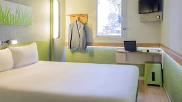 Een hotelkamer met een bed, een bureau met een laptop, een televisie en een raam met uitzicht op bomen.