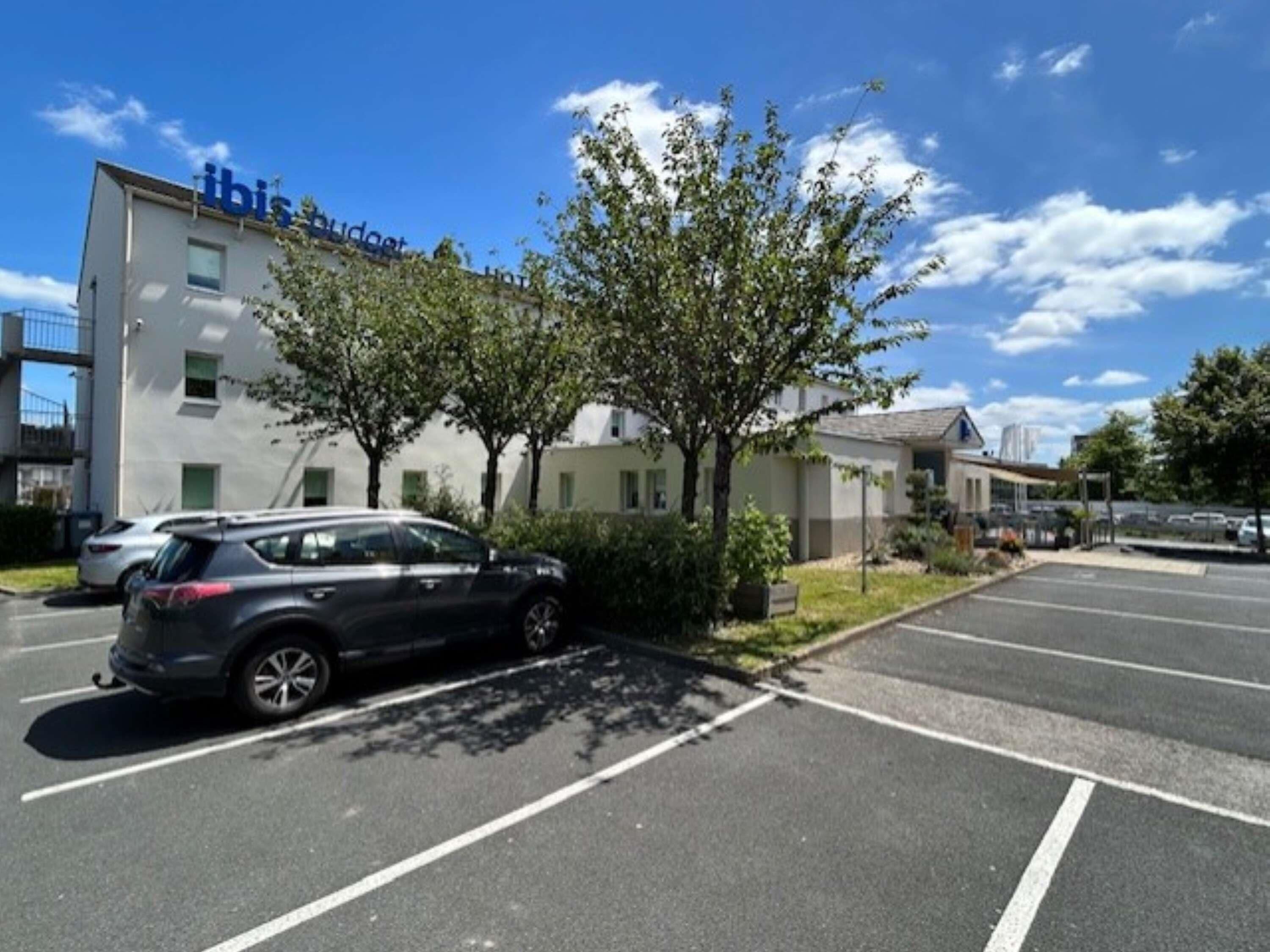 Un parking avec, au fond, un bâtiment sur lequel on peut lire l’inscription « ibis budget hotel ».