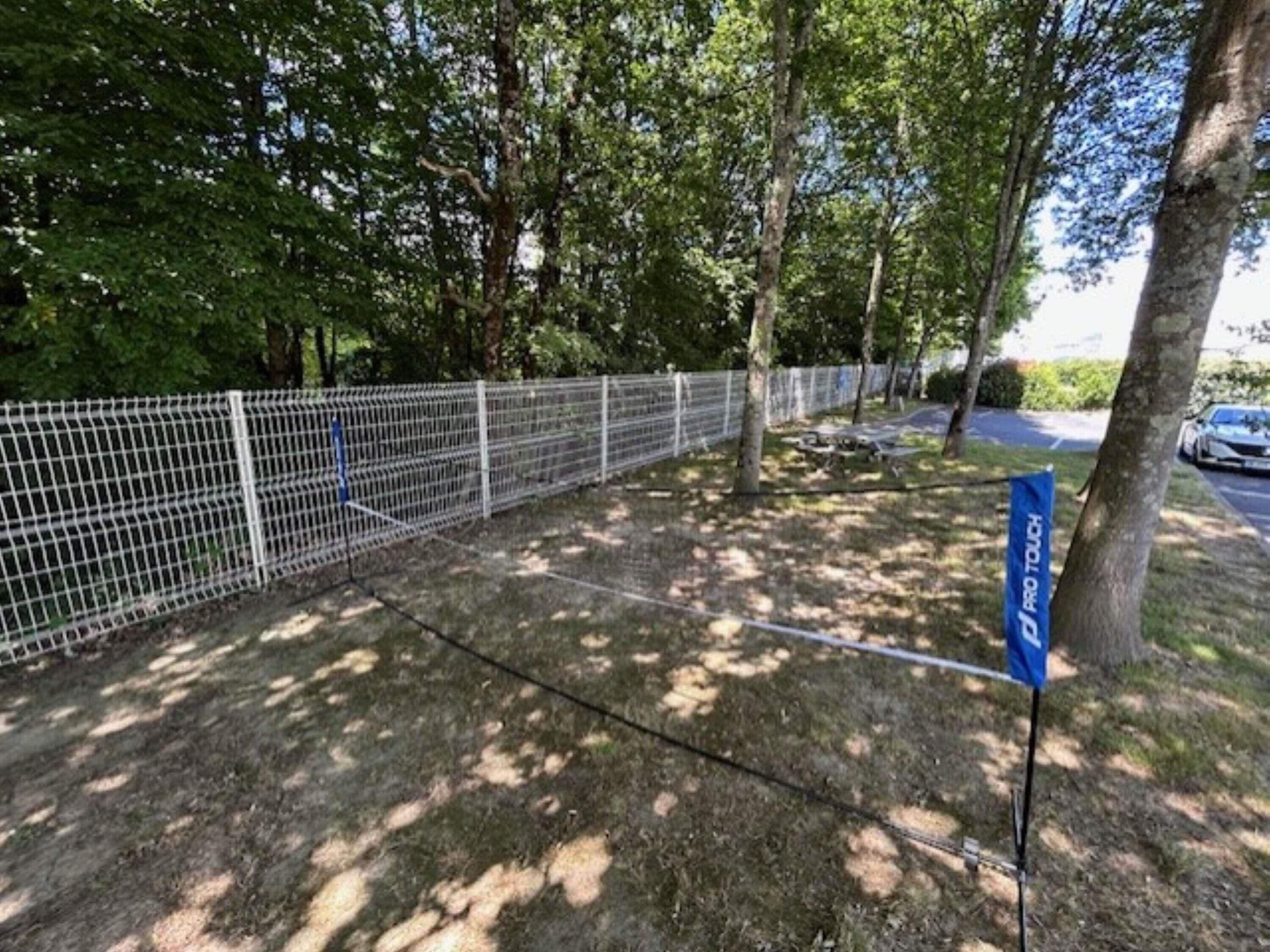 Een omheind buitengebied met bomen en een blauw bord.