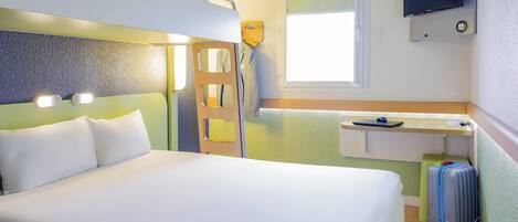 Habitación de hotel con literas, un escritorio con silla, televisor montado en la pared y una maleta en el suelo.
