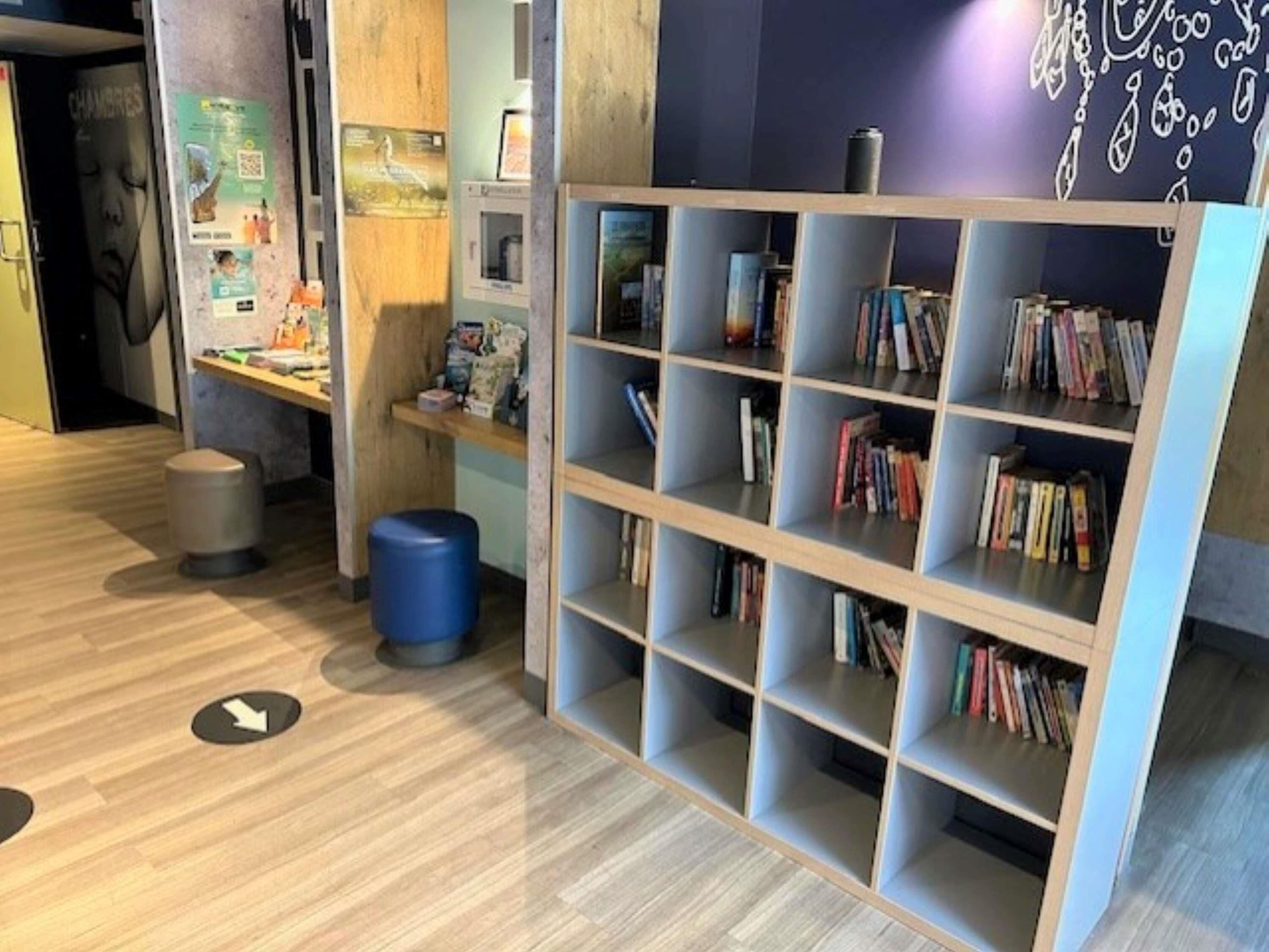 A library with bookshelves, a trash bin, and a wall with decorative elements.