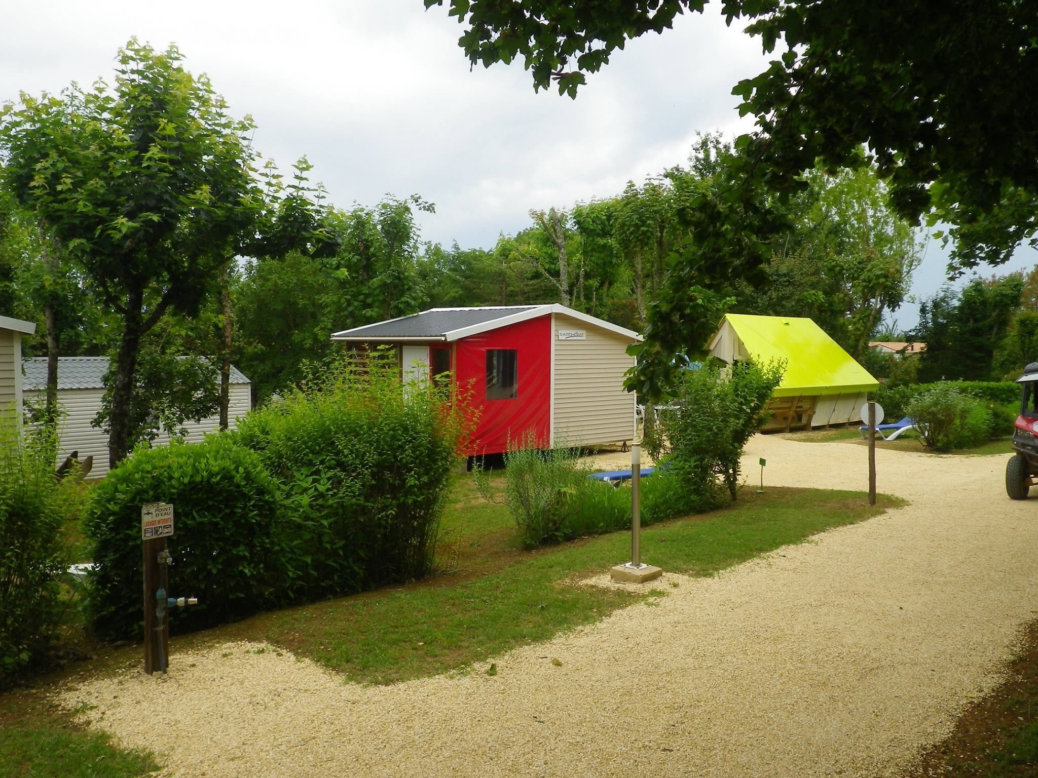 A campsite with a red and yellow tent, surrounded by greenery and a gravel path.