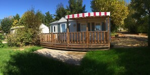 A mobile home with a wooden deck and a red and white awning. - Camping Les Poutiroux - Mobilhome (Limeuil)