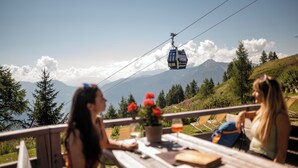 A scenic outdoor seating area with a view of a mountain and a cable car in the background. - Hotel Gasthaus Post (Campo di Trens)