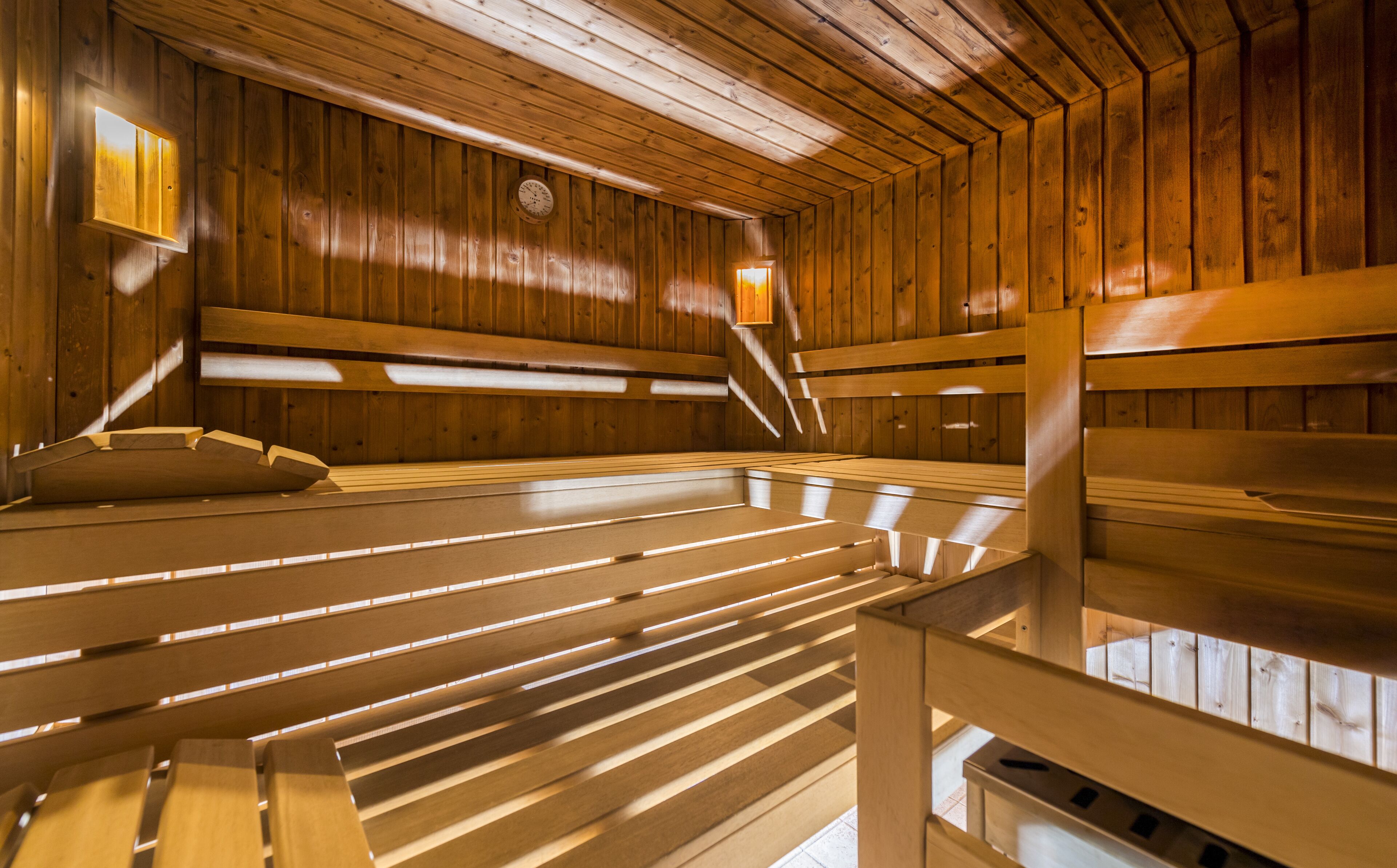 A sauna with wooden benches and slatted floors, wooden walls, and two wall-mounted lights.