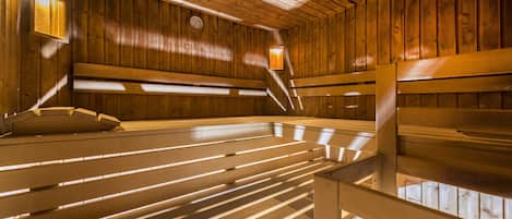 A sauna with wooden benches and slatted floors, wooden walls, and two wall-mounted lights.