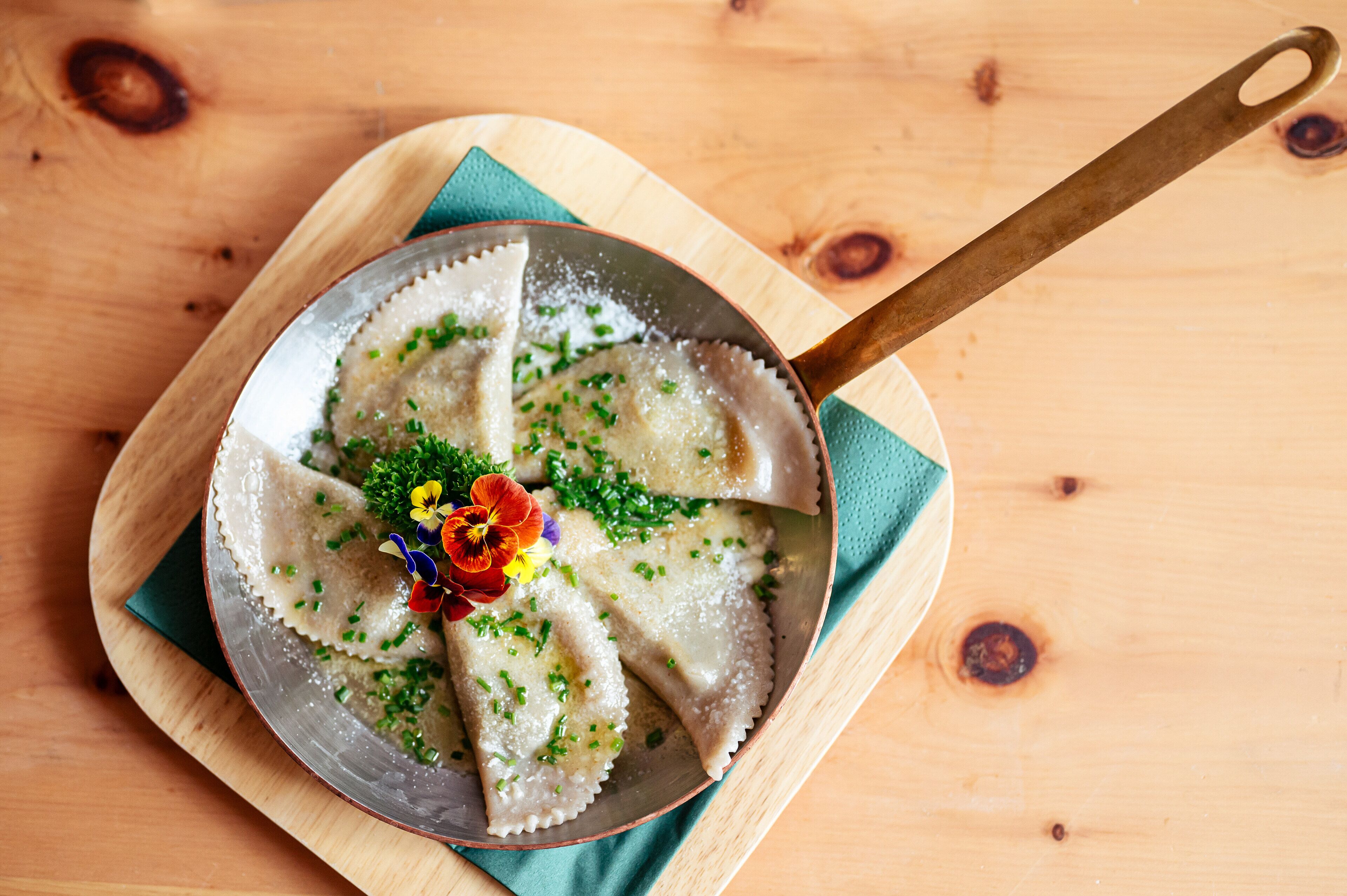 A pan of ravioli garnished with herbs and flowers on a wooden board.
