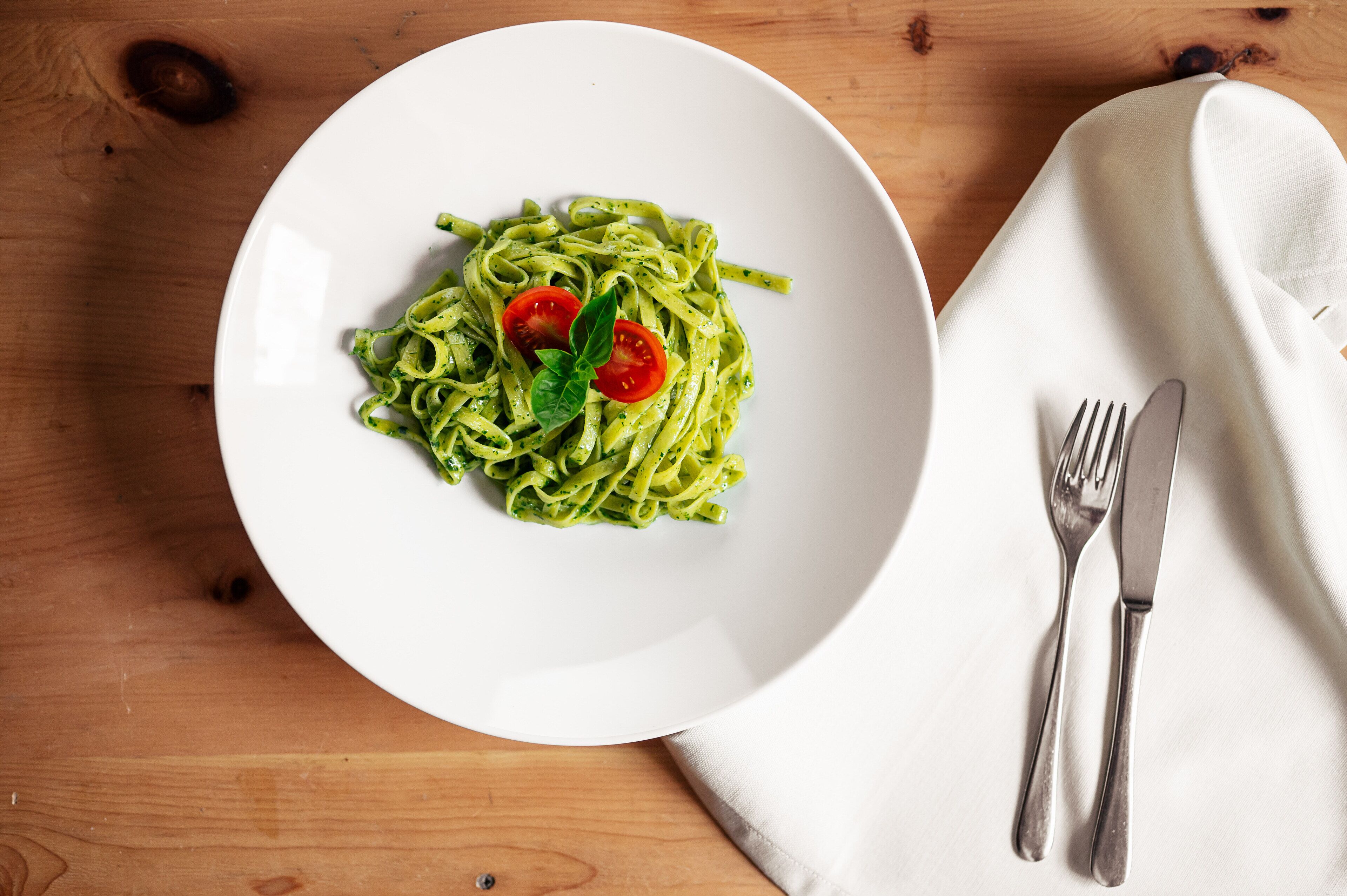 Une assiette de pâtes, garnie de tomates cerises et de basilic, posée sur une table en bois.