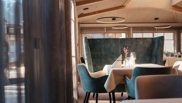 A dining area with a table set for two, featuring a dark green upholstered chair and a light-colored tablecloth. - Hotel Gasthaus Post (Campo di Trens)