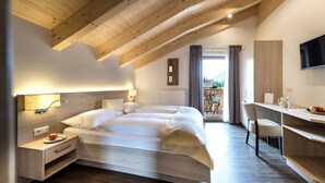 A modern bedroom with a loft-style ceiling, a bed, bedside tables, a desk, and a view of the outdoors. - Hotel Gasthaus Post (Campo di Trens)